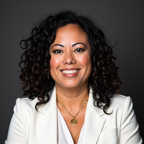 liesl-perez-chief-growth-officer-axis-integrated-mental-health-colorado Smiling woman with curly dark hair wearing a white blazer and gold necklace against a dark background.